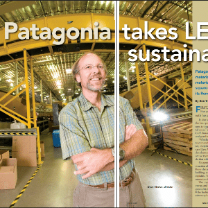 A man stands smiling in a warehouse with yellow shelving and industrial lighting, as part of a feature on Patagonia’s sustainability efforts.