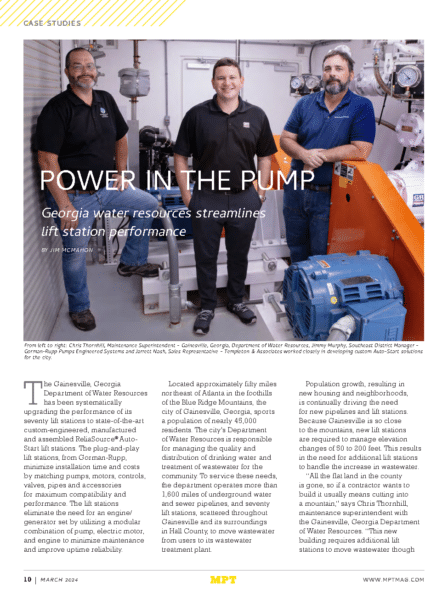 Three men stand in a water pump facility, posing next to large industrial pumps and control panels.